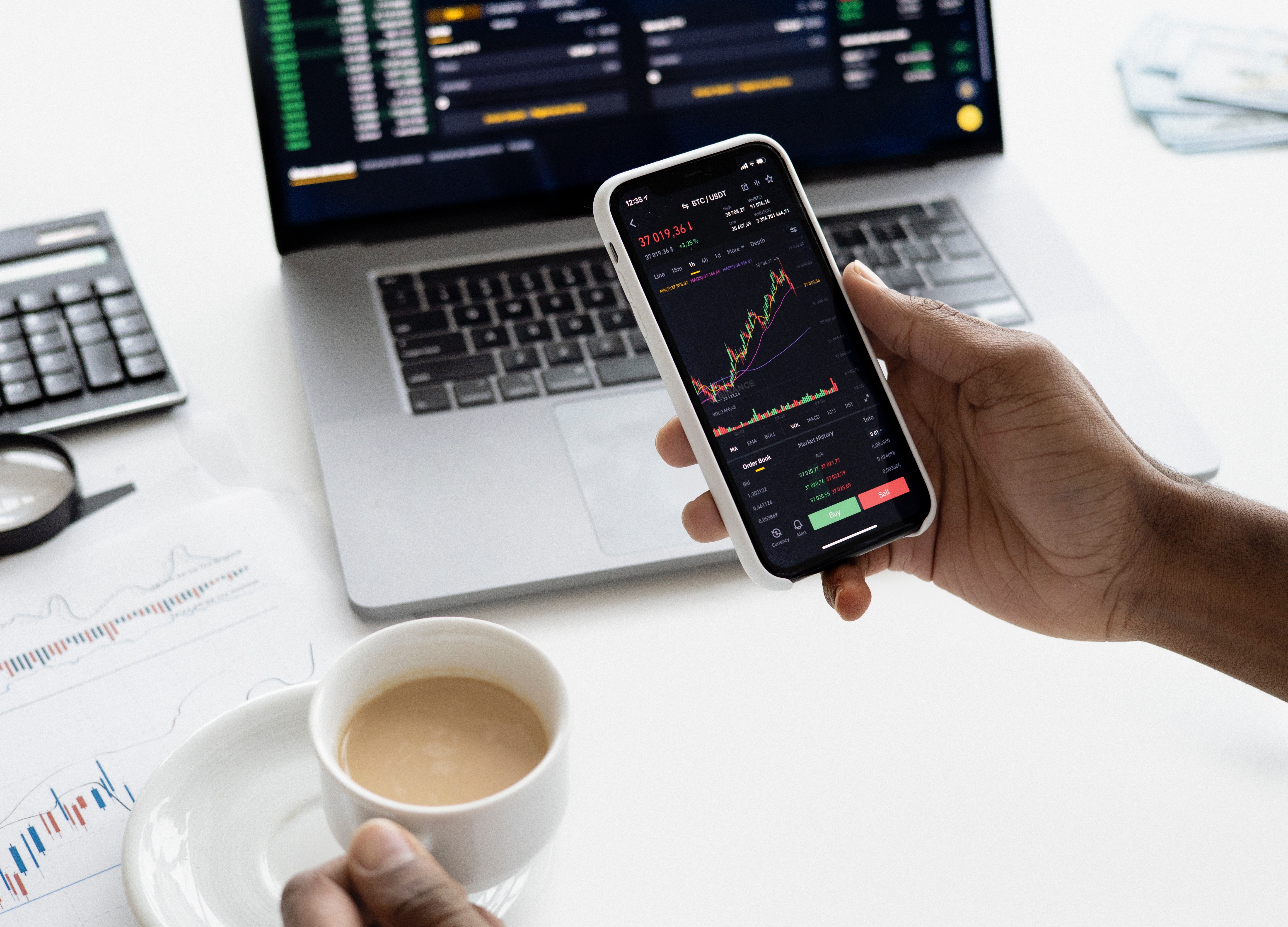 Trading on a phone beside a laptop